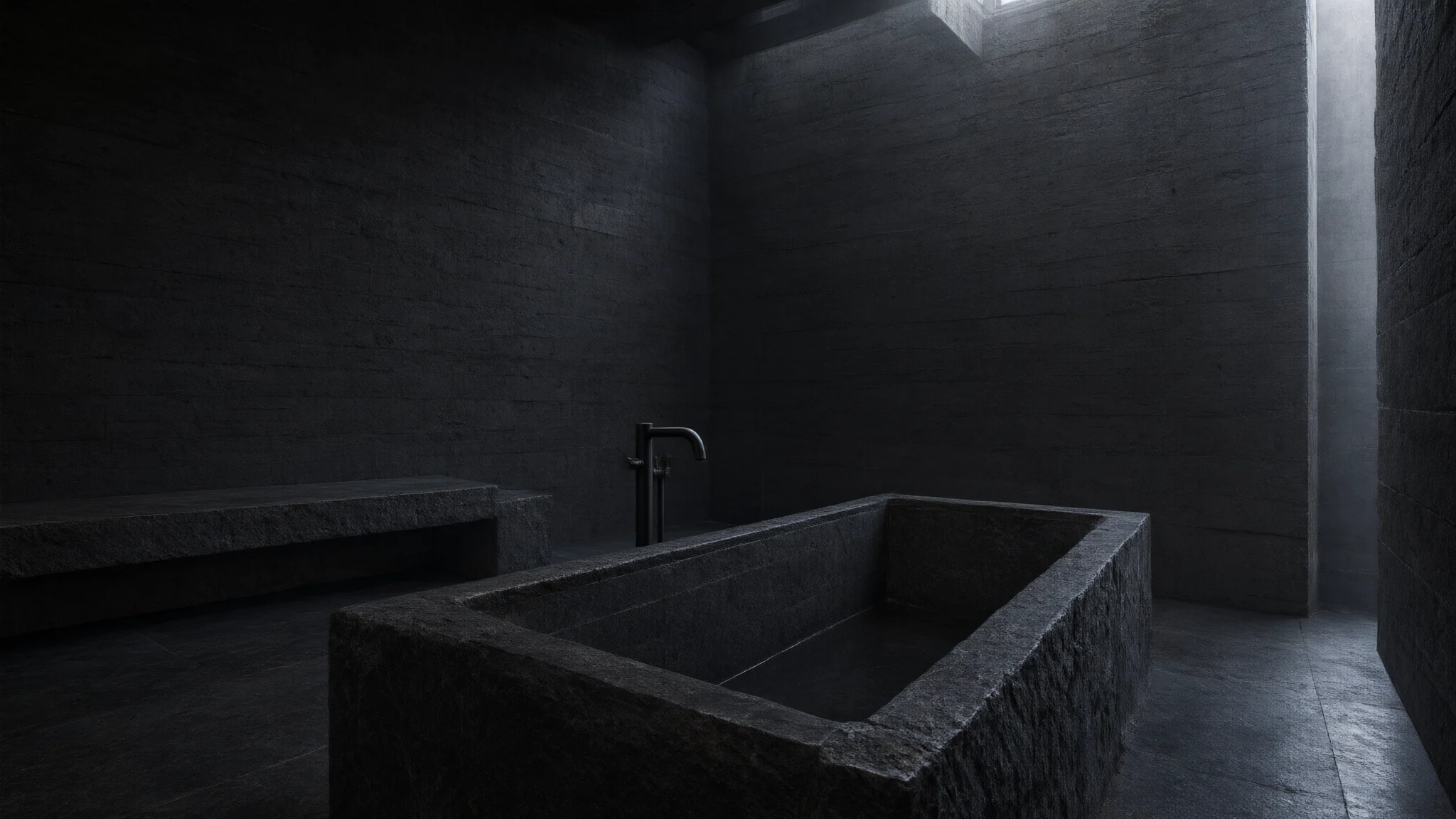 Bain brutaliste en basalte sombre, baignoire monolithique et lumière argentée.